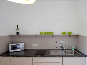 Una cucina compatta con un forno a microonde, una bottiglia di vino e un lavandino.