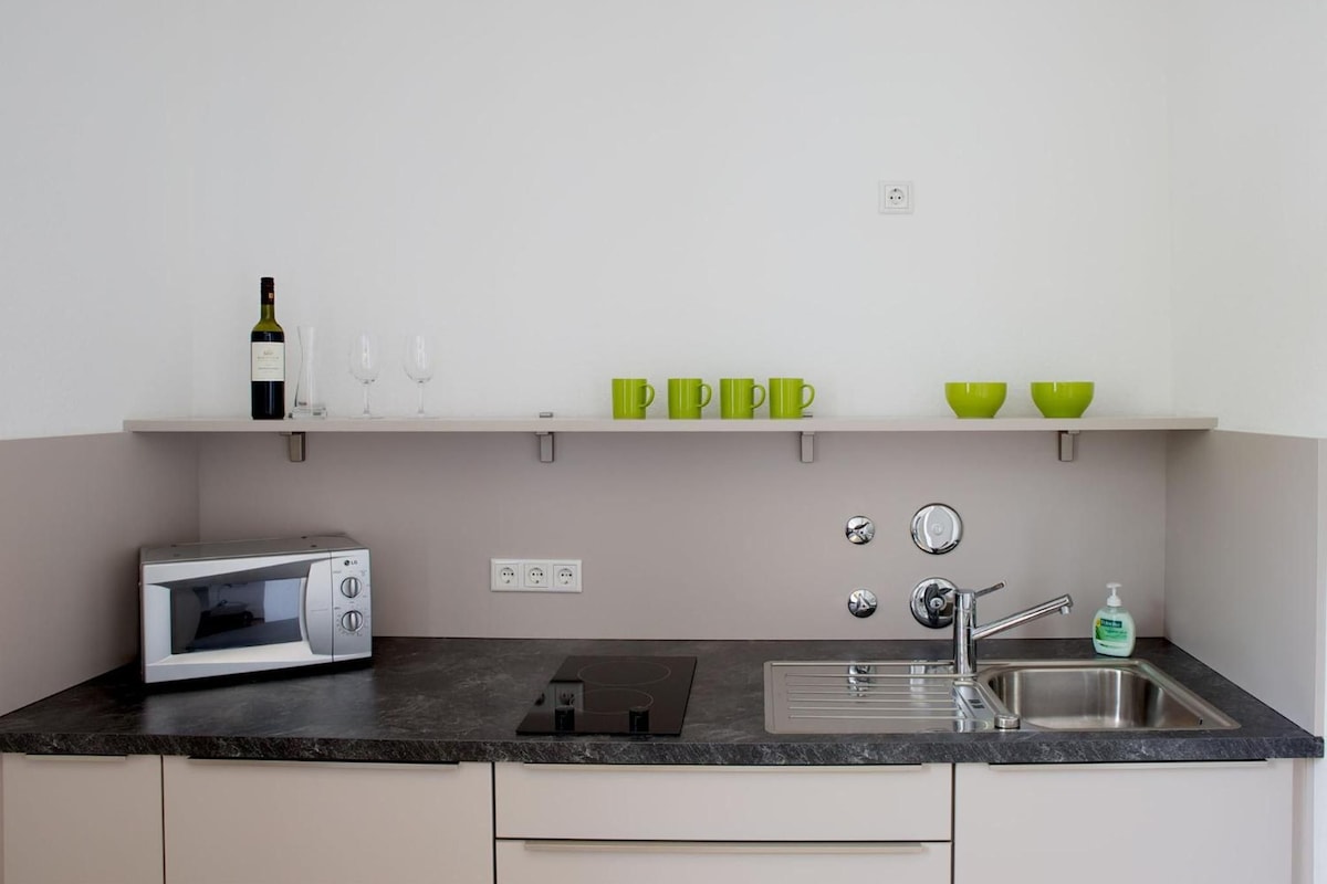 A modern kitchen with a microwave, sink, and a wine bottle on the counter.