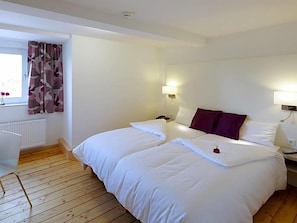 A hotel room with two beds, a window with curtains, a radiator, and wall-mounted lamps.