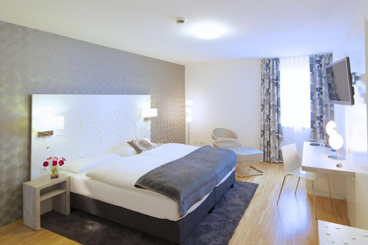 A modern hotel room with a large bed, bedside tables, a desk, and a TV.