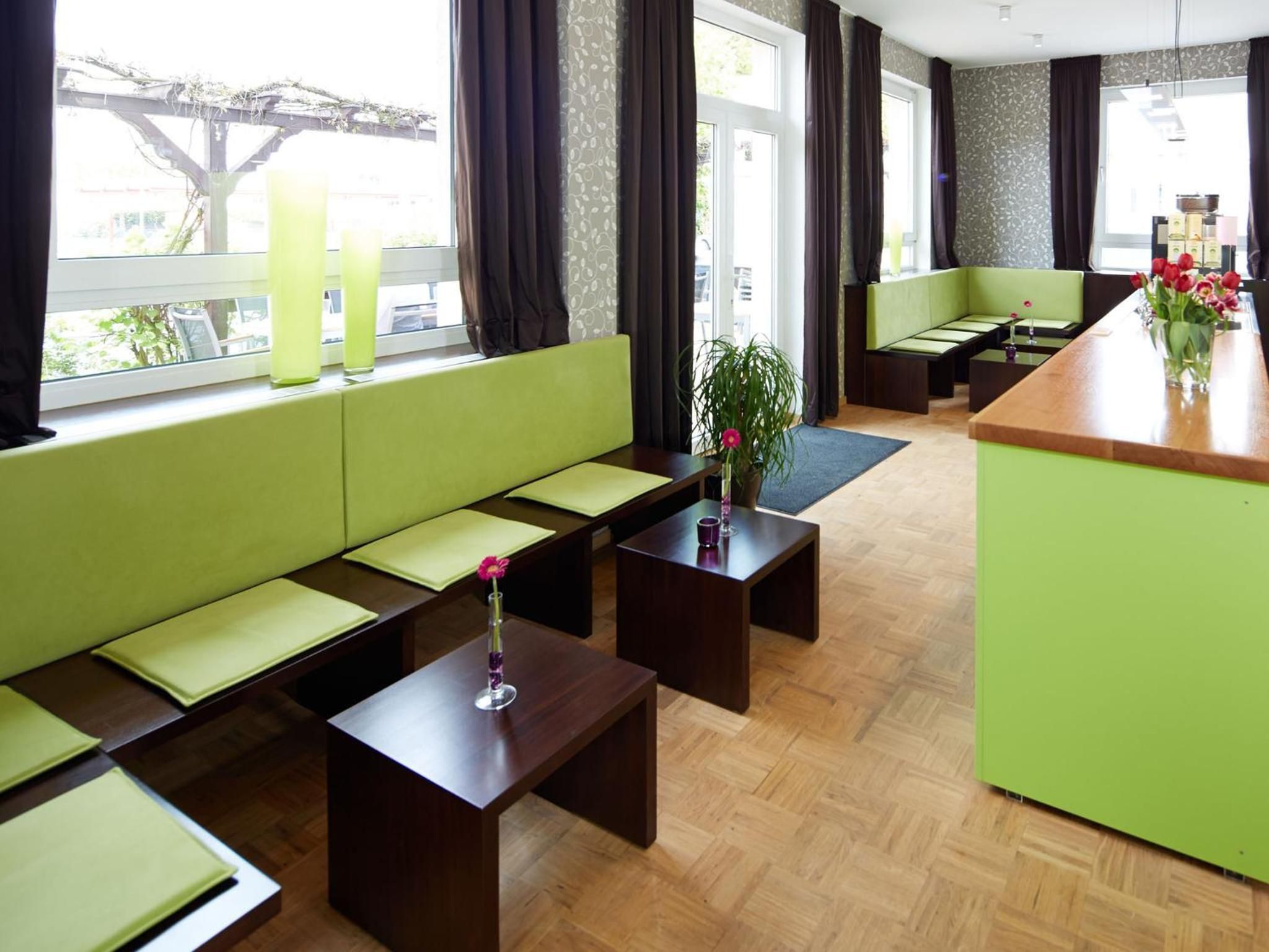 A modern hotel lobby with a green sofa, wooden tables, and a bar area.