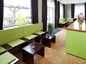 A modern hotel lobby with a green sofa, wooden tables, and a bar area.