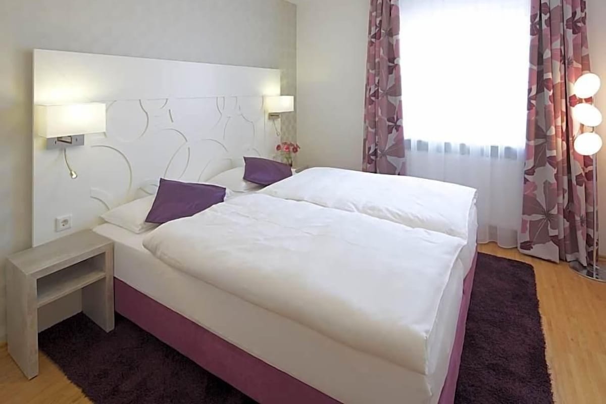 Camera d'albergo con un letto matrimoniale, lampade sui comodini, un comodino e una finestra con tende.