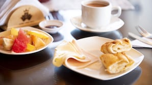 A dining table with a plate of fruit, a cup of coffee, and a pastry.