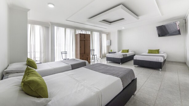 A hotel room with three beds, a TV mounted on the wall, and a large window with curtains. - Hotel Elegant Suite (Bogotá)