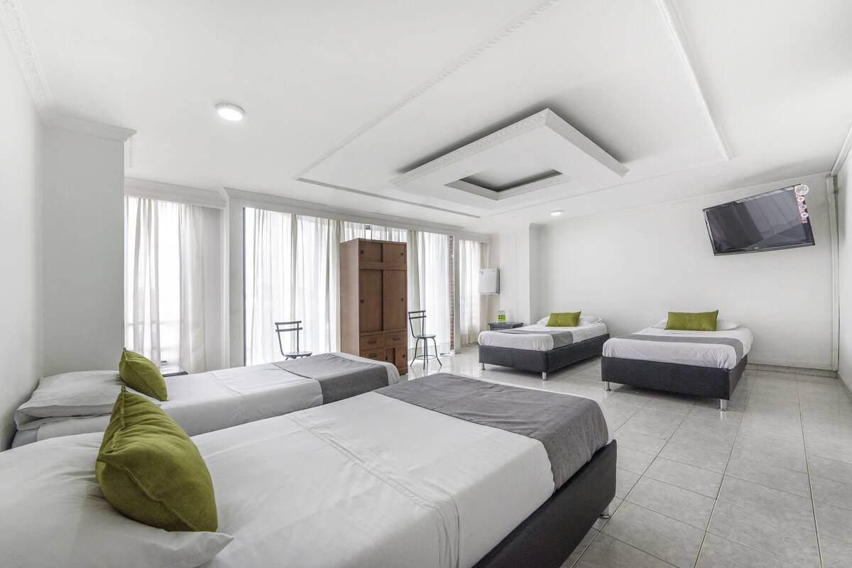 A hotel room with three beds, a TV mounted on the wall, and a large window with curtains.