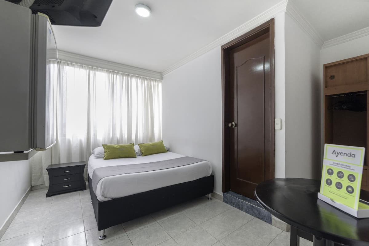 A hotel room with a bed, a nightstand, a desk, a wardrobe, and a signboard.