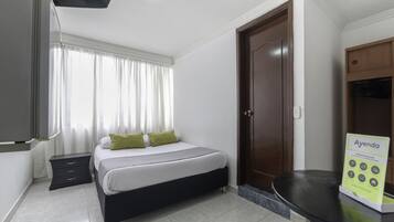 A hotel room with a bed, a nightstand, a desk, a wardrobe, and a signboard.