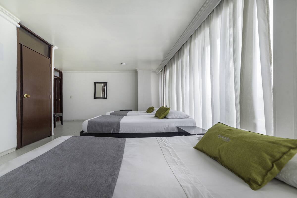 A hotel room with two beds, a large window with curtains, a door, and a framed picture on the wall.
