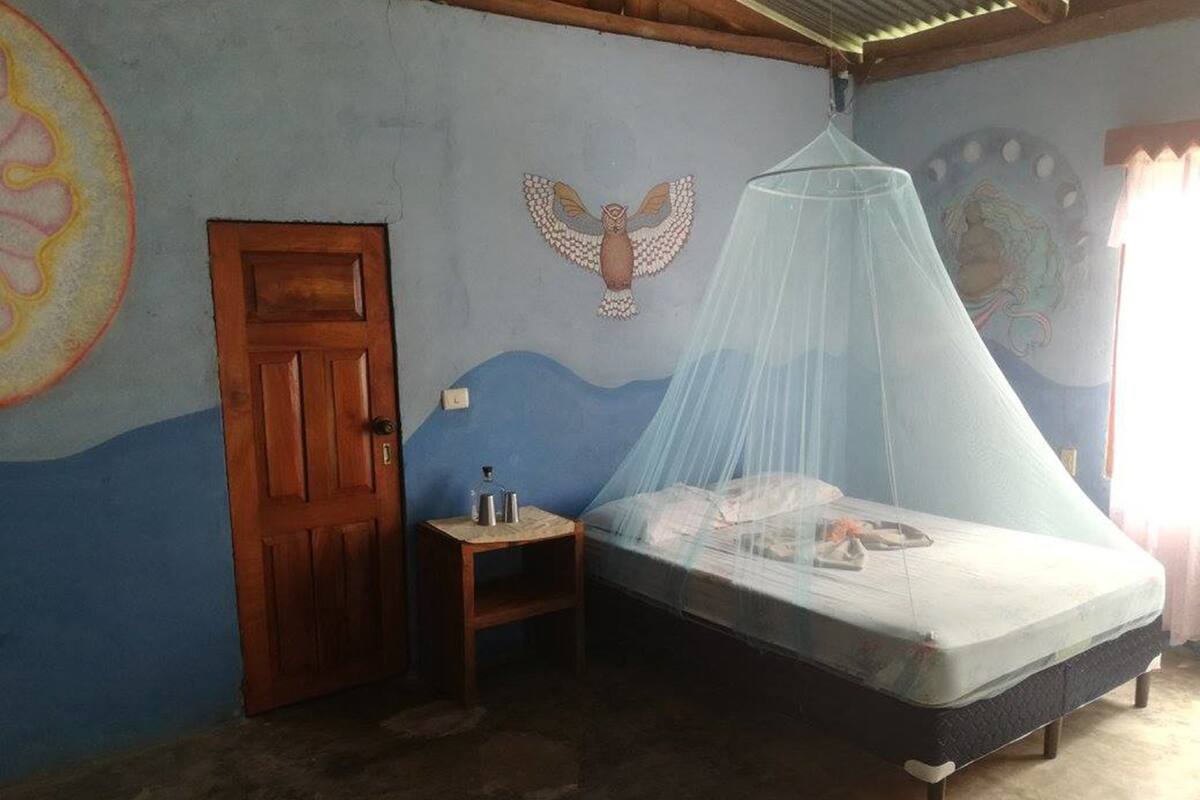A bedroom with a bed under a mosquito net, a wooden door, and a small table with items on it.