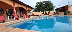 A swimming pool with a tiled edge, surrounded by a wooden deck and red lounge chairs. - Villa Calhau (São Luís)