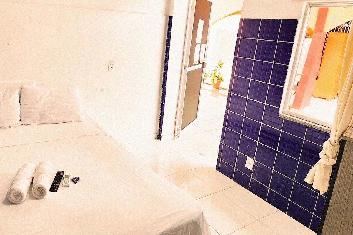 Ein Hotelzimmer mit Bett, einem Badezimmer mit blauen Fliesen und einem Fenster mit Vorhängen.