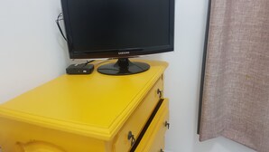 Et Samsung fjernsyn på en gul kommode med skuffer, foran en hvid væg.