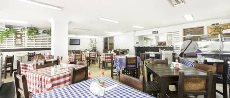 Un restaurante con manteles a cuadros, sillas de madera y una zona de cocina.