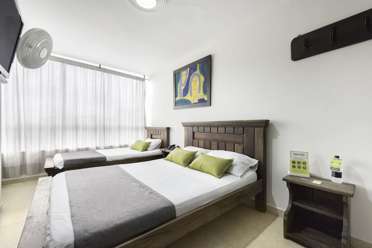 Quarto de hotel com duas camas, um ventilador de teto, um quadro, um mini-bar e uma placa com informações sobre os serviços.