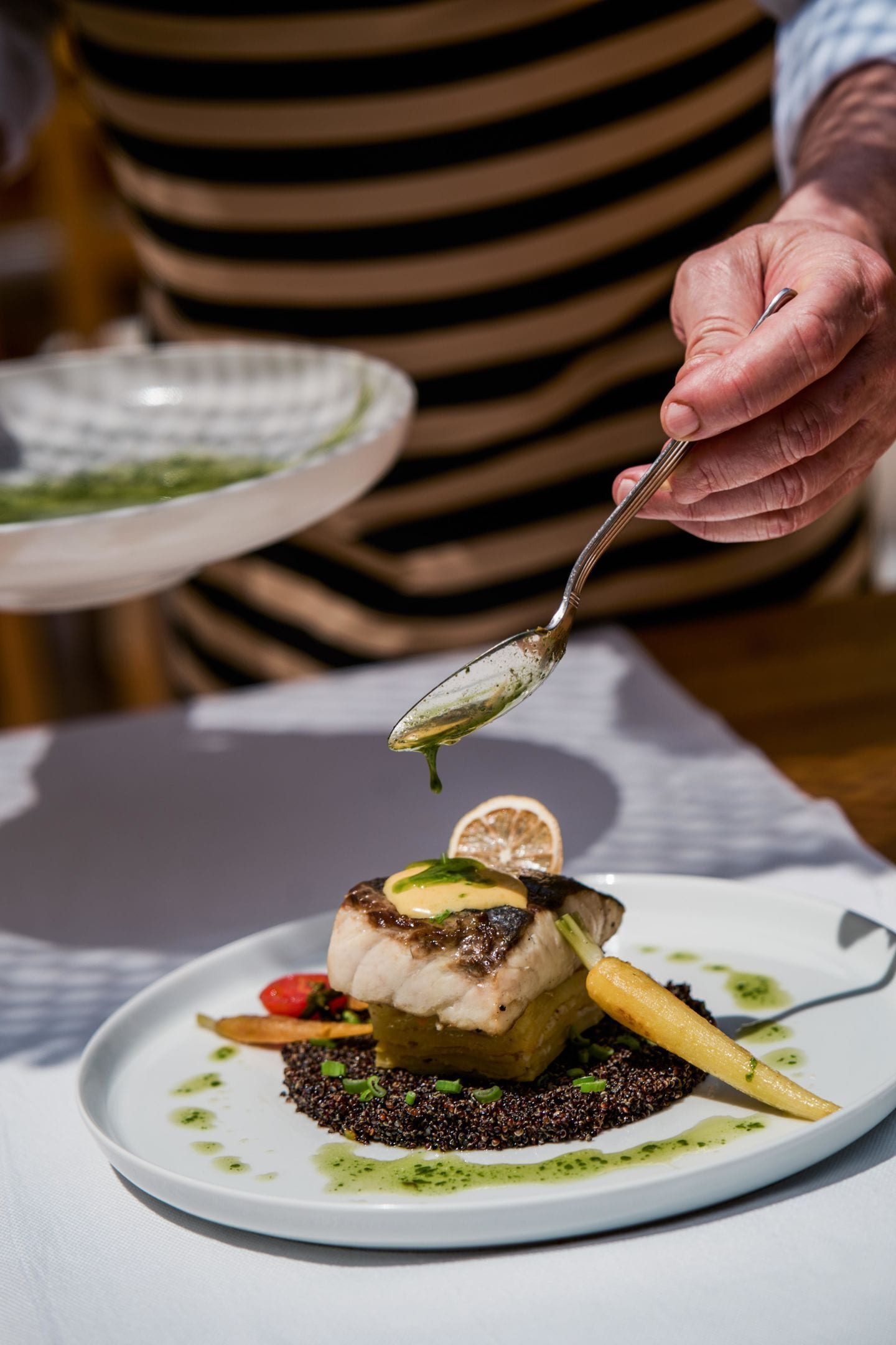 A person serving a dish with a spoon on a white plate.