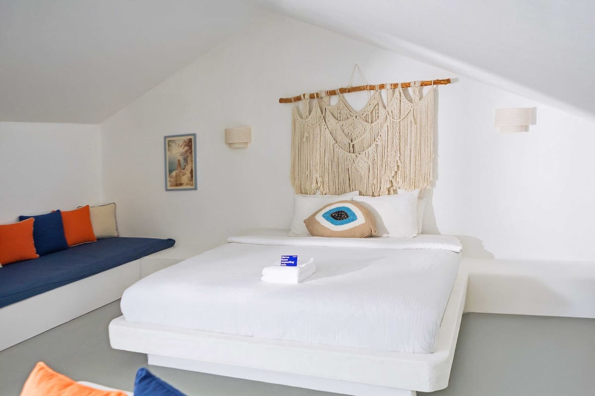 A bedroom with a bed, a macrame wall hanging, a framed picture, and a sofa with cushions.