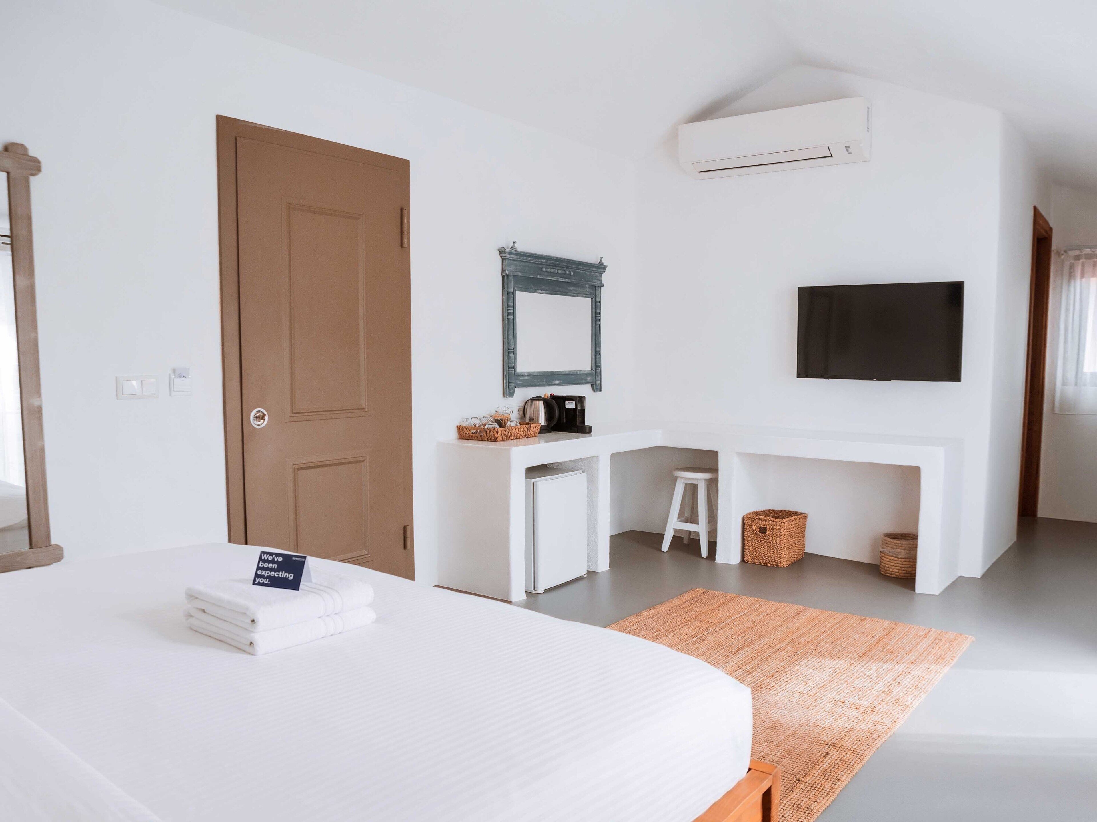 A hotel room with a bed, a desk, a chair, a television, and an air conditioning unit.