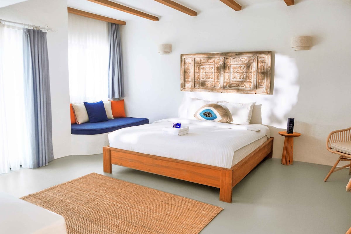 A bedroom with a wooden bed, a window seat with cushions, a bedside table, and a wall-mounted artwork.