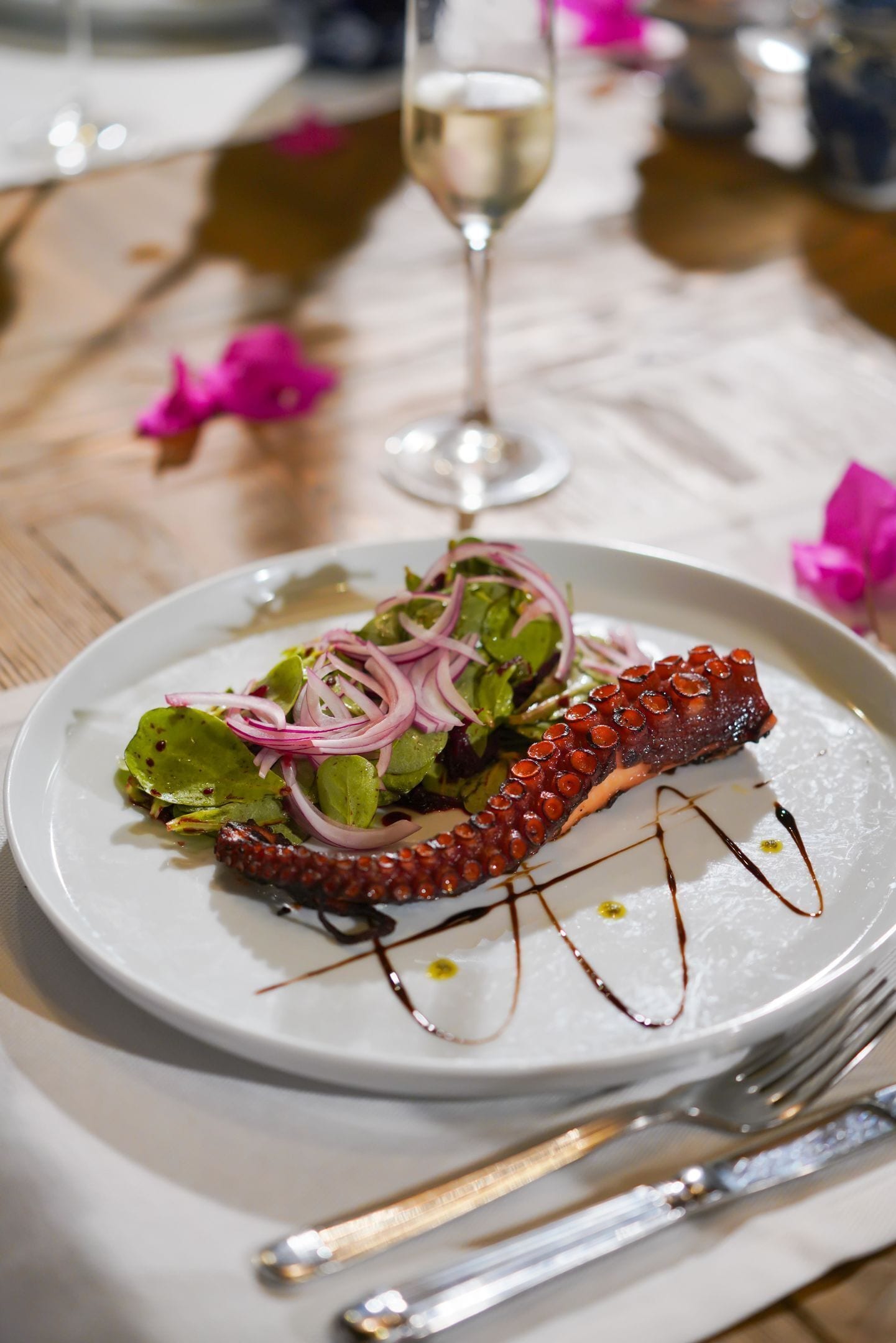 A plate with octopus, salad, and sauce on a white plate.