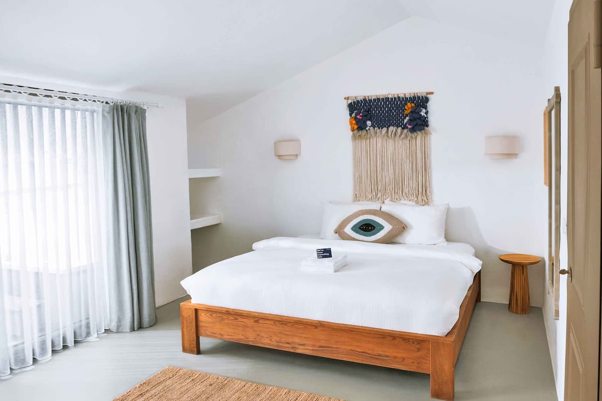 A neatly arranged bedroom with a wooden bed, a wall-mounted macrame piece, and a bedside table.