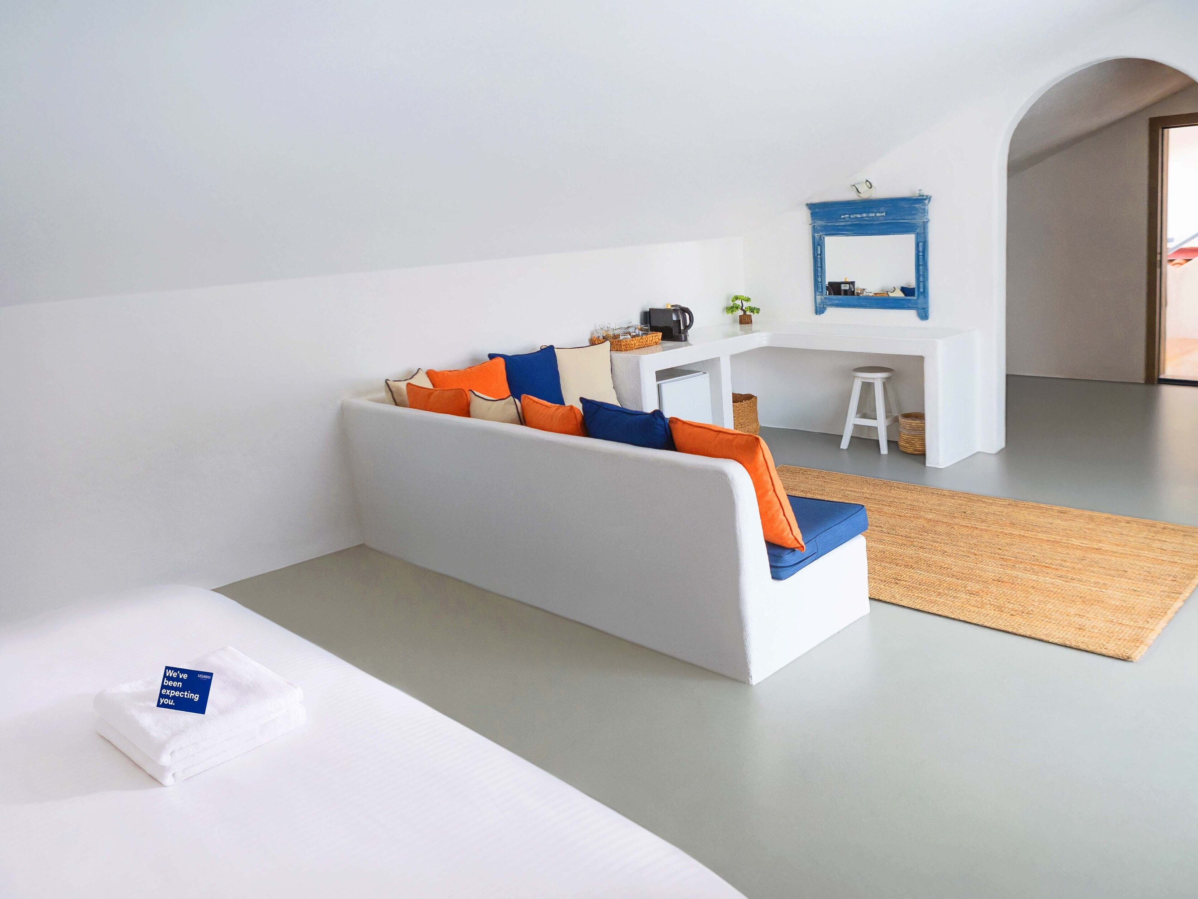 A modern living room with a white sofa, a small white desk, a blue-framed mirror, and a woven rug.