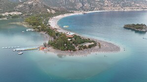 An aerial view of a coastal area with a beach, boats, and a small island with buildings and trees. - Kassandra Ölüdeniz  (Fethiye)