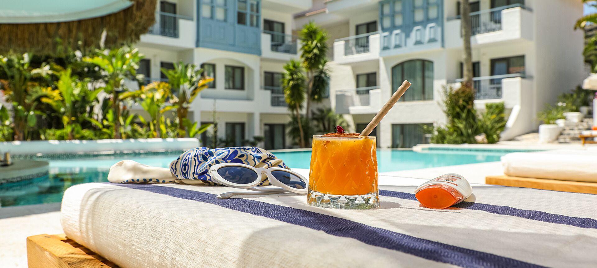 A poolside setting with a glass of orange juice, sunglasses, and a towel on a lounge chair.