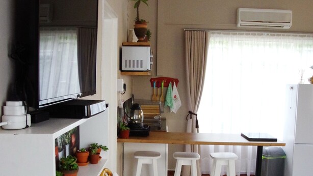 Quarto de hotel pequeno com cama, televisão fixada na parede, cozinha compacta e área de refeições.