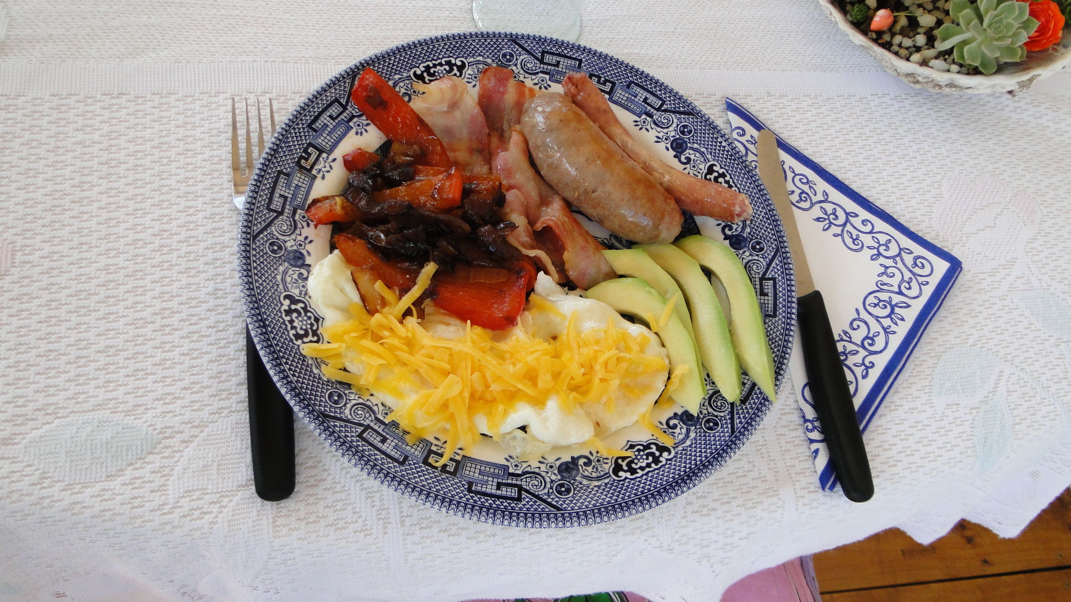 A plate of breakfast food including eggs, bacon, avocado, and cheese on a patterned plate.