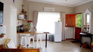 Uma cozinha compacta com geladeira, mesa de madeira e banquetas brancas.