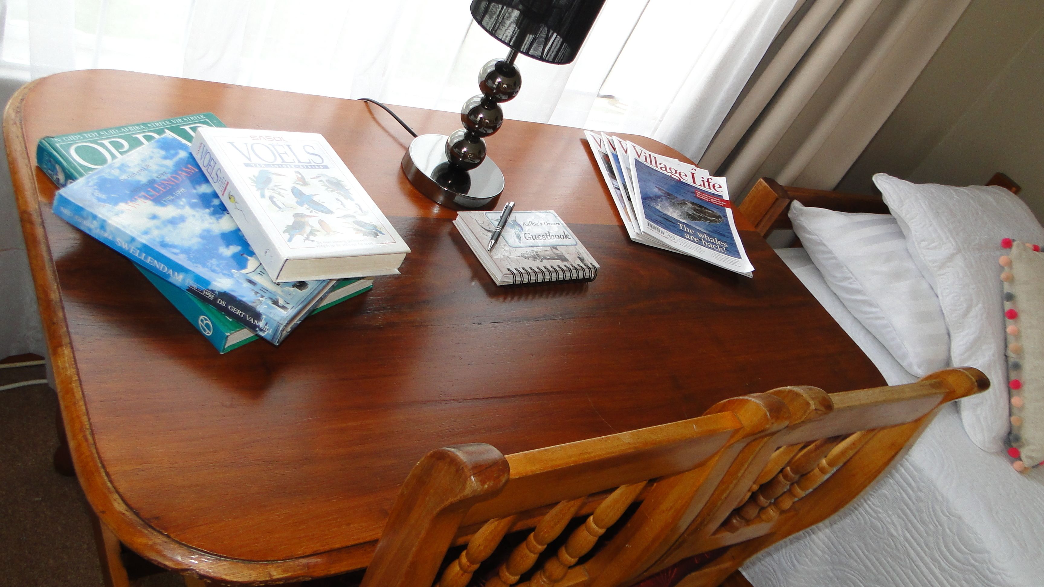 A wooden dining table with books, a lamp, and a notebook.