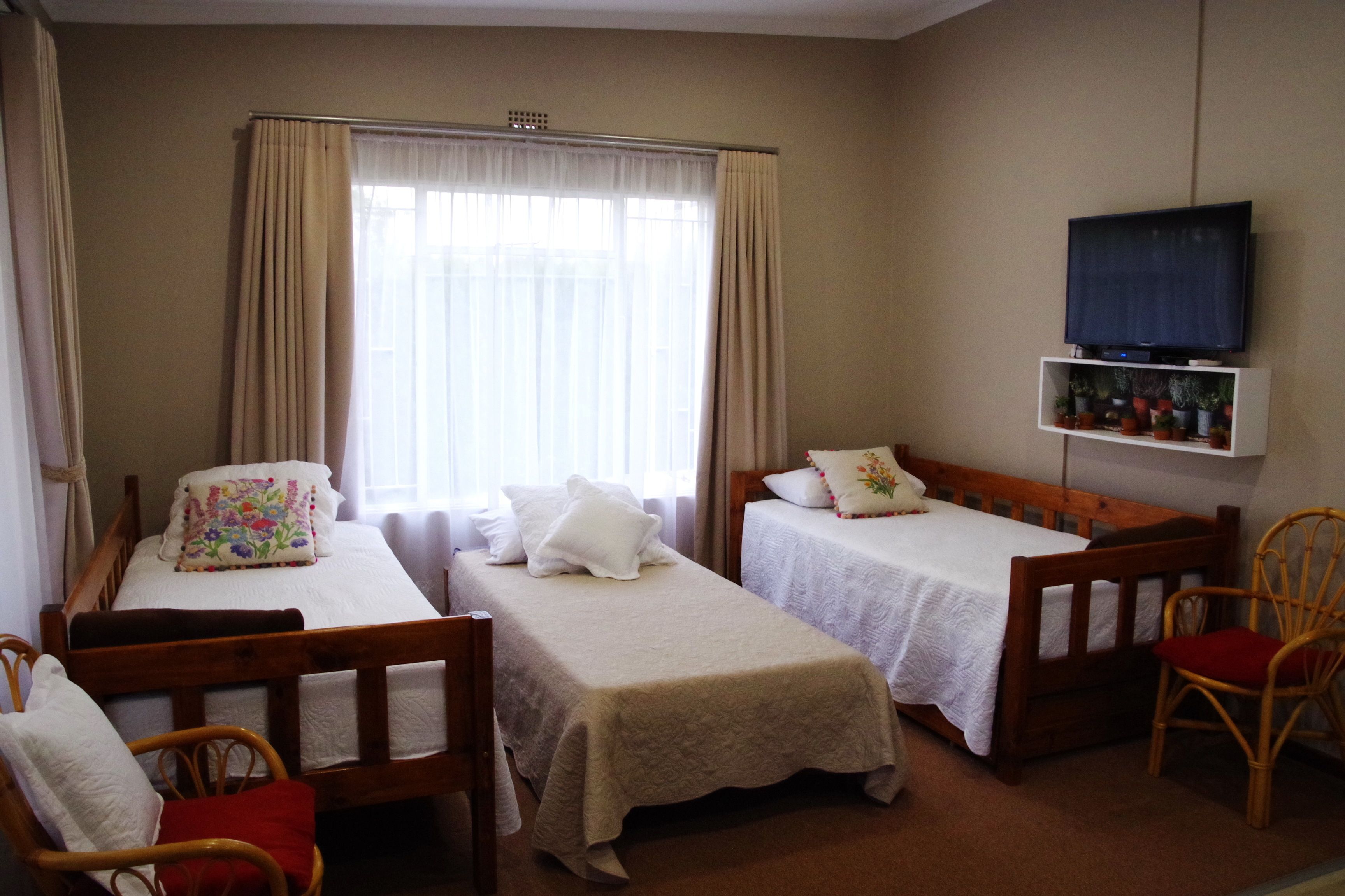 A hotel room with two single beds, a television on a shelf, and a window with curtains.