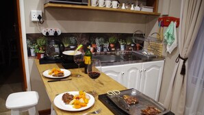 Uma cozinha com bancada de madeira, pia e diversos eletrodomésticos. Há pratos com comida e uma garrafa de vinho na bancada.
