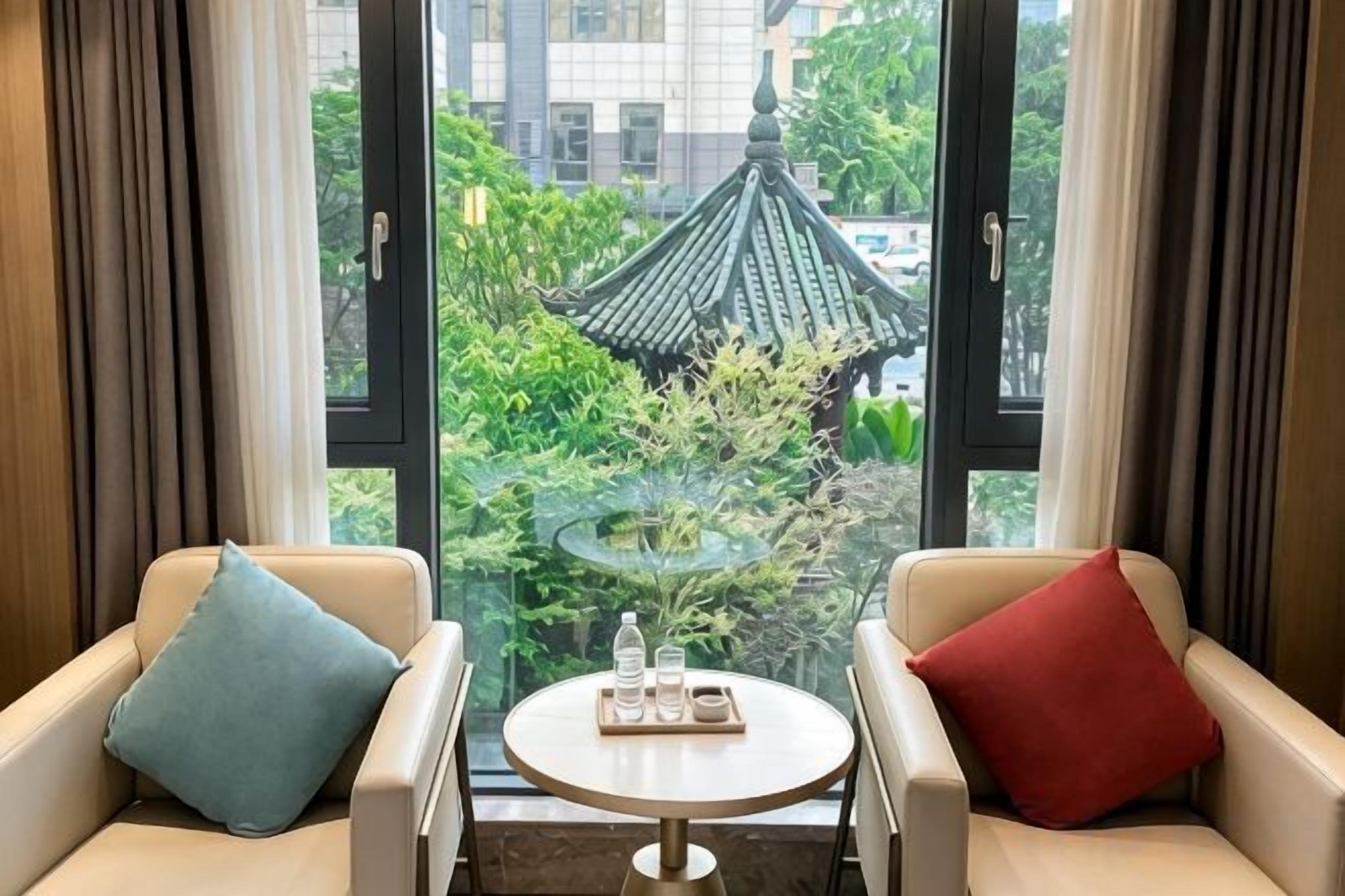 A room with two sofas facing a small table with a tray of items, a window with a view of a traditional building and greenery.