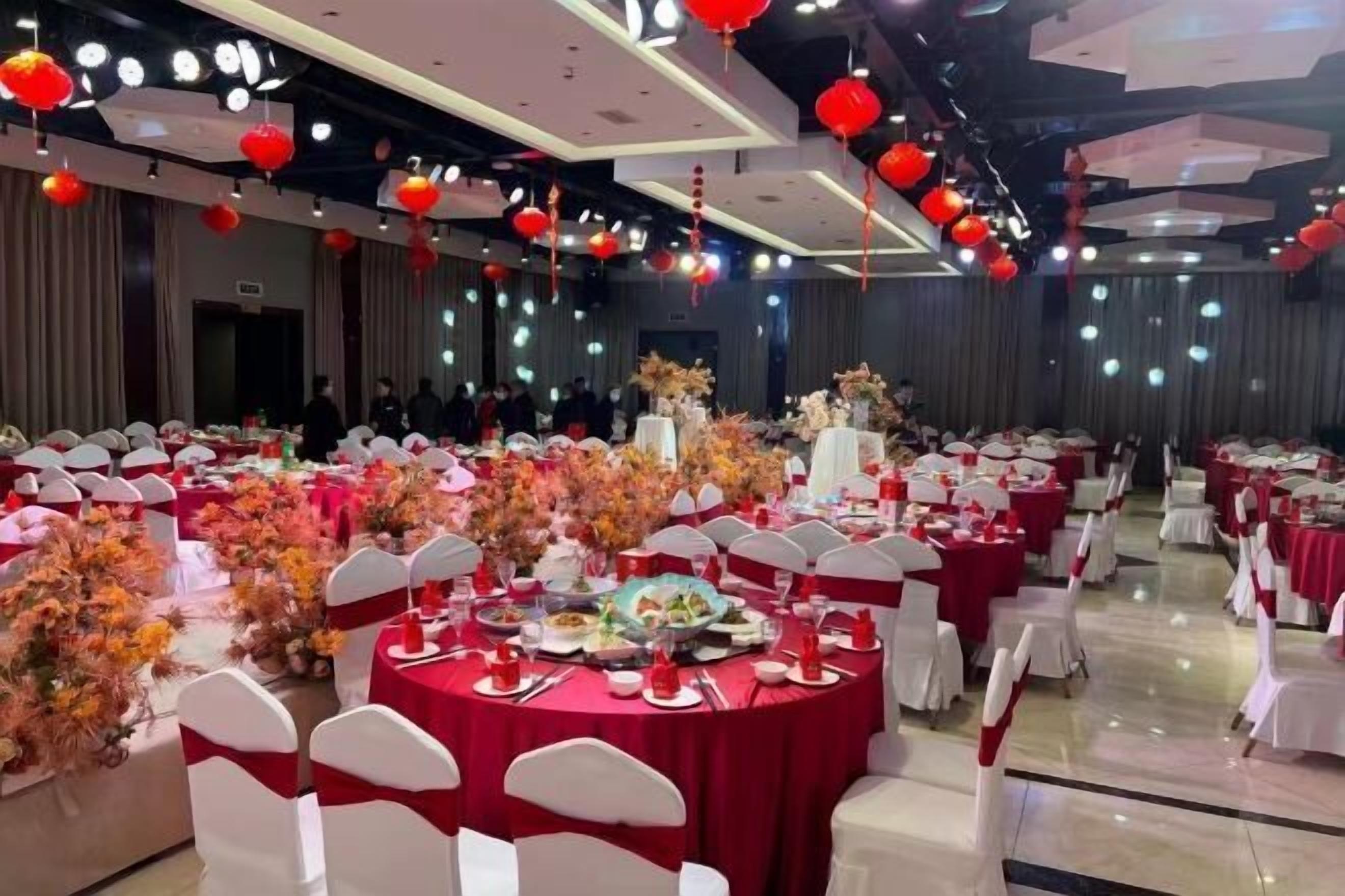 Een feestzaal met ronde tafels, witte stoelen en rode decoraties.