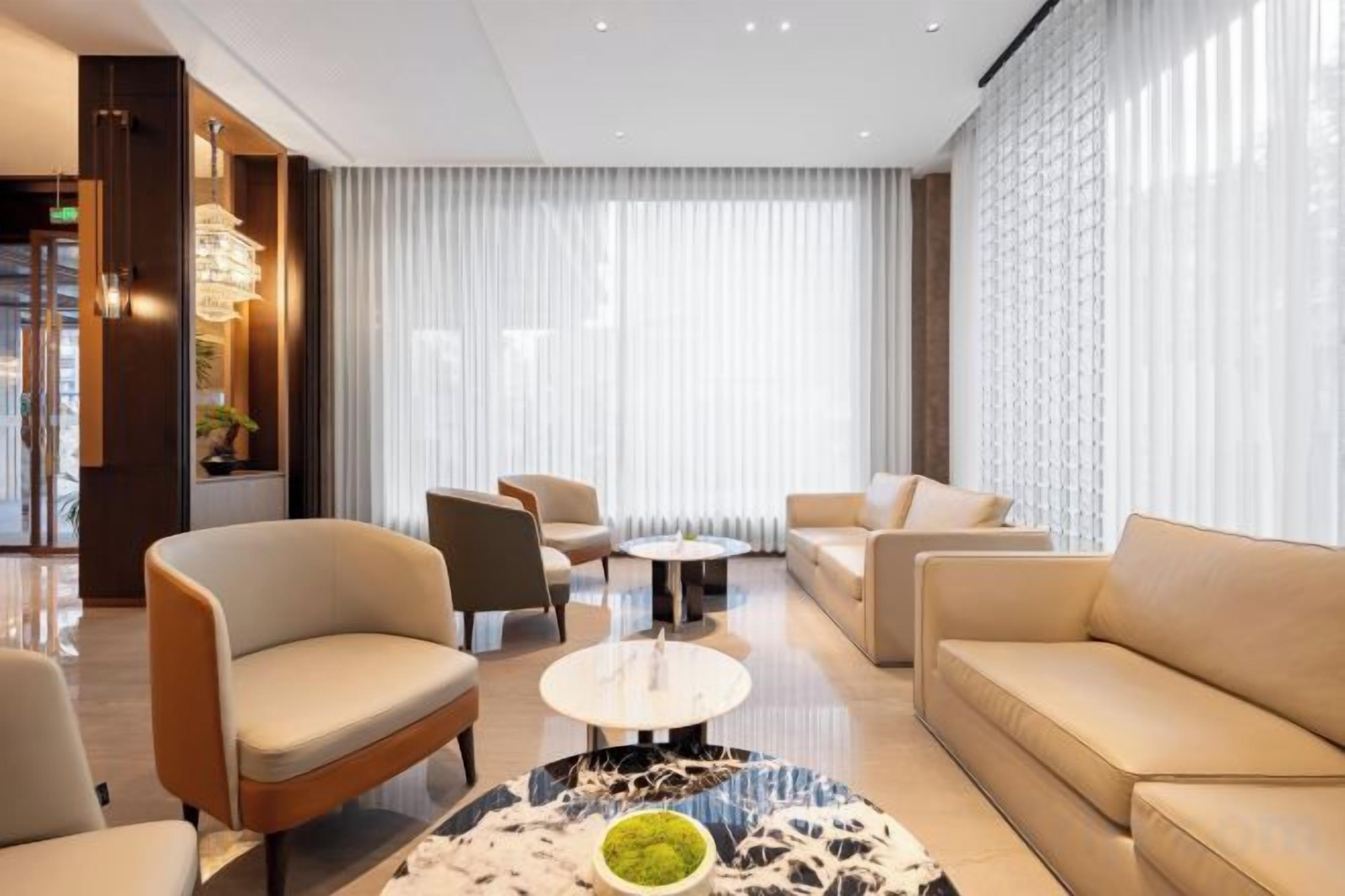 Un hall d’hôtel moderne avec un espace salon, une table basse et une grande fenêtre avec des rideaux.