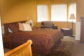 A bedroom with a large bed, a chair, a nightstand, and a lamp. - Telles House (Angel Fire)