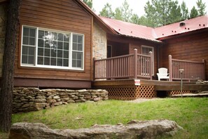 A wooden cabin with a stone foundation, a porch with a railing, and a white chair. - Telles House (Angel Fire)