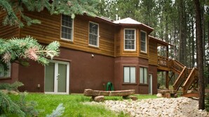 Une cabane avec une façade en bois, une porte d’entrée, un escalier menant à une terrasse, et une forêt environnante.