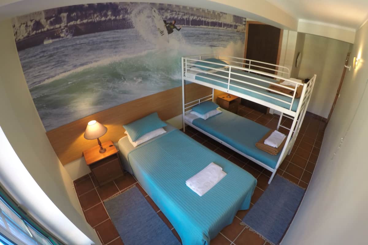 A room with bunk beds, a nightstand with a lamp, a wall mural of a surfer, and a tiled floor.
