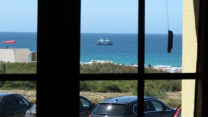 Vista a través de una ventana que muestra una zona costera con un barco en el agua, coches estacionados y un edificio con una bandera.