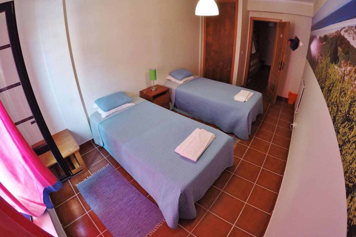 A room with two beds, a wooden wardrobe, a green nightstand, and a purple rug.