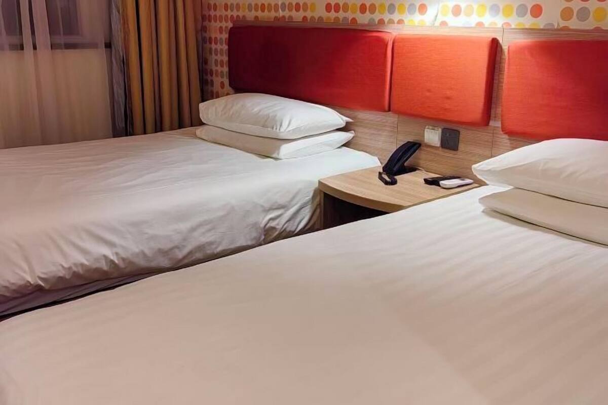 A hotel room with two beds, a bedside table with a phone, and a wall with a polka dot pattern.