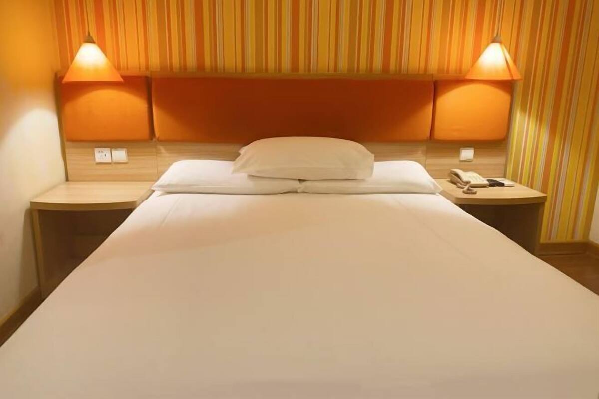A hotel room with a single bed, two bedside tables, and a striped headboard.