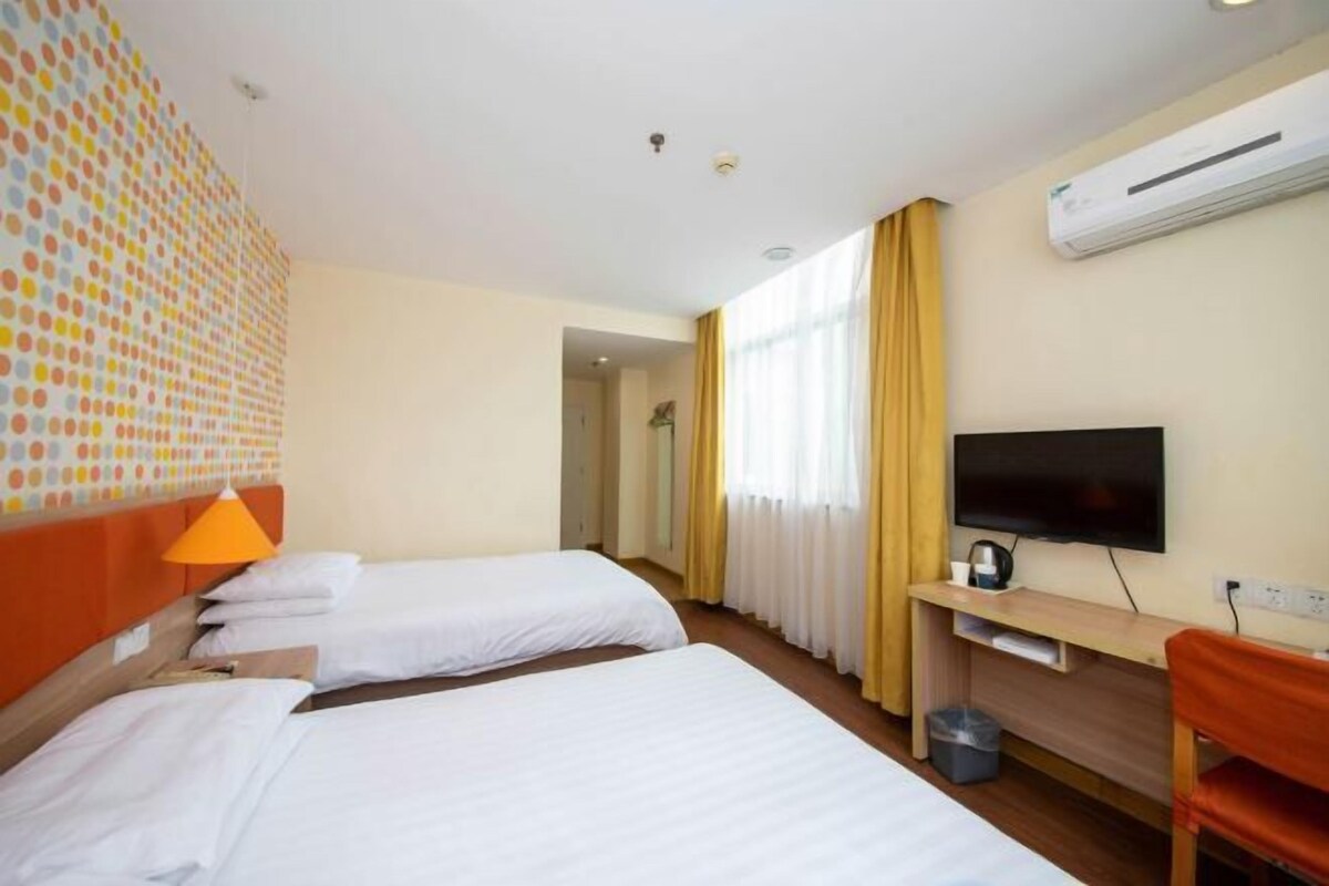 A hotel room with two beds, a TV, a desk, and an air conditioning unit.