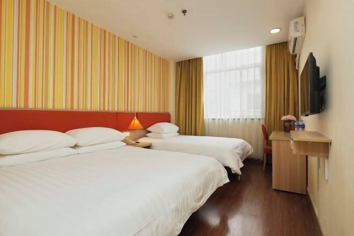 A hotel room with two beds, a desk, a TV, and a window with curtains.