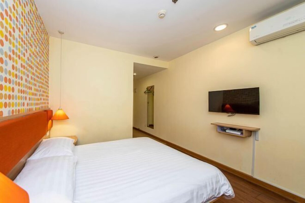 A hotel room with a bed, a TV mounted on the wall, and an air conditioning unit.