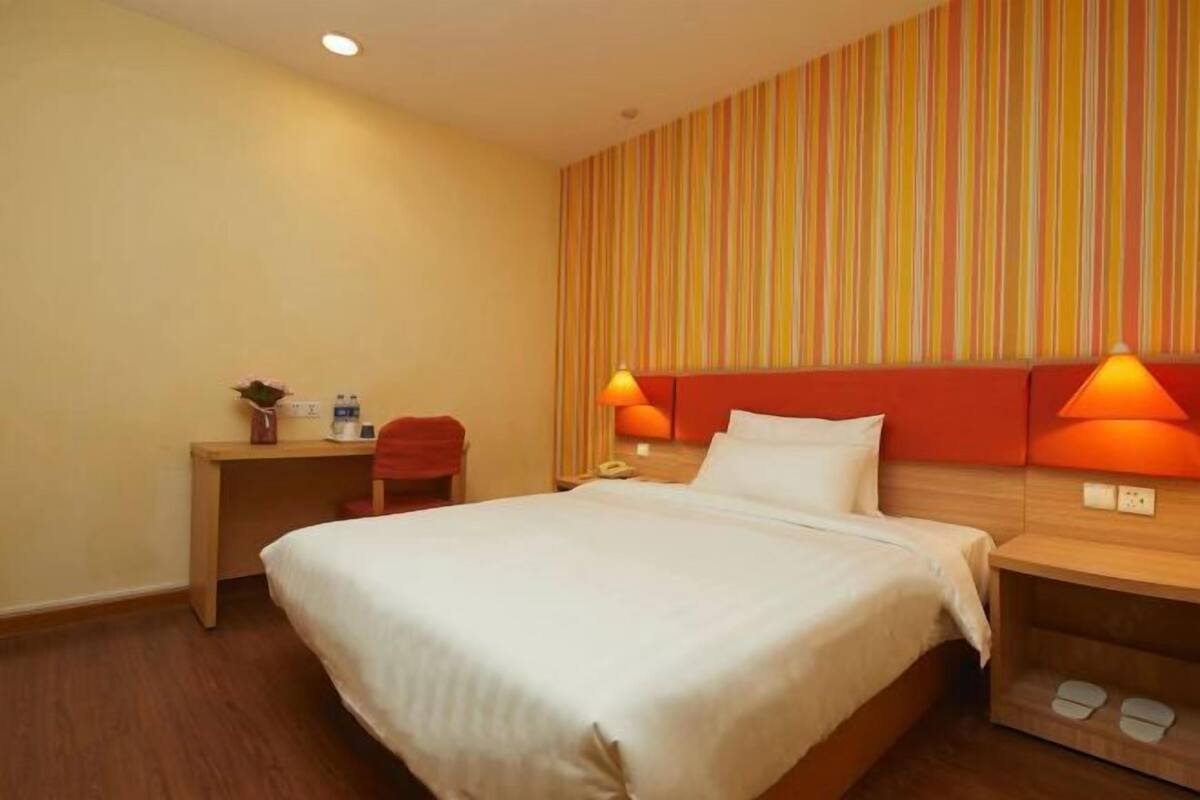 A hotel room with a bed, bedside table, lamp, and a striped wall.