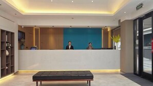 A modern reception area with a reception desk, two staff members, a seating area, and a plant. - Homeinn Hotel (Yangzhou Shouxihu Wenchang Pavilion) (Yangzhou)